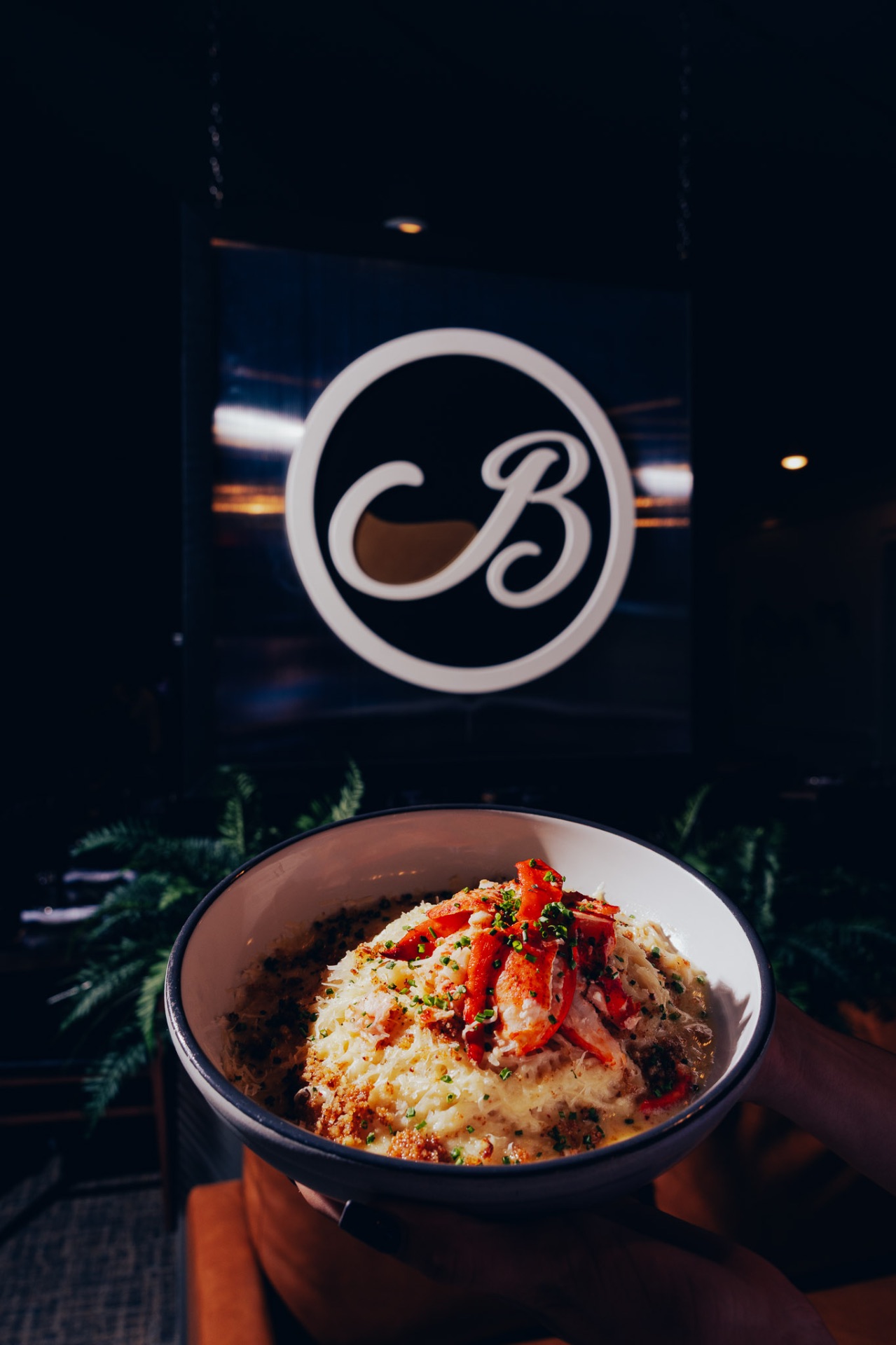 Lobster pasta held in front of the White Wine & Butter B logo sign in Greer, SC