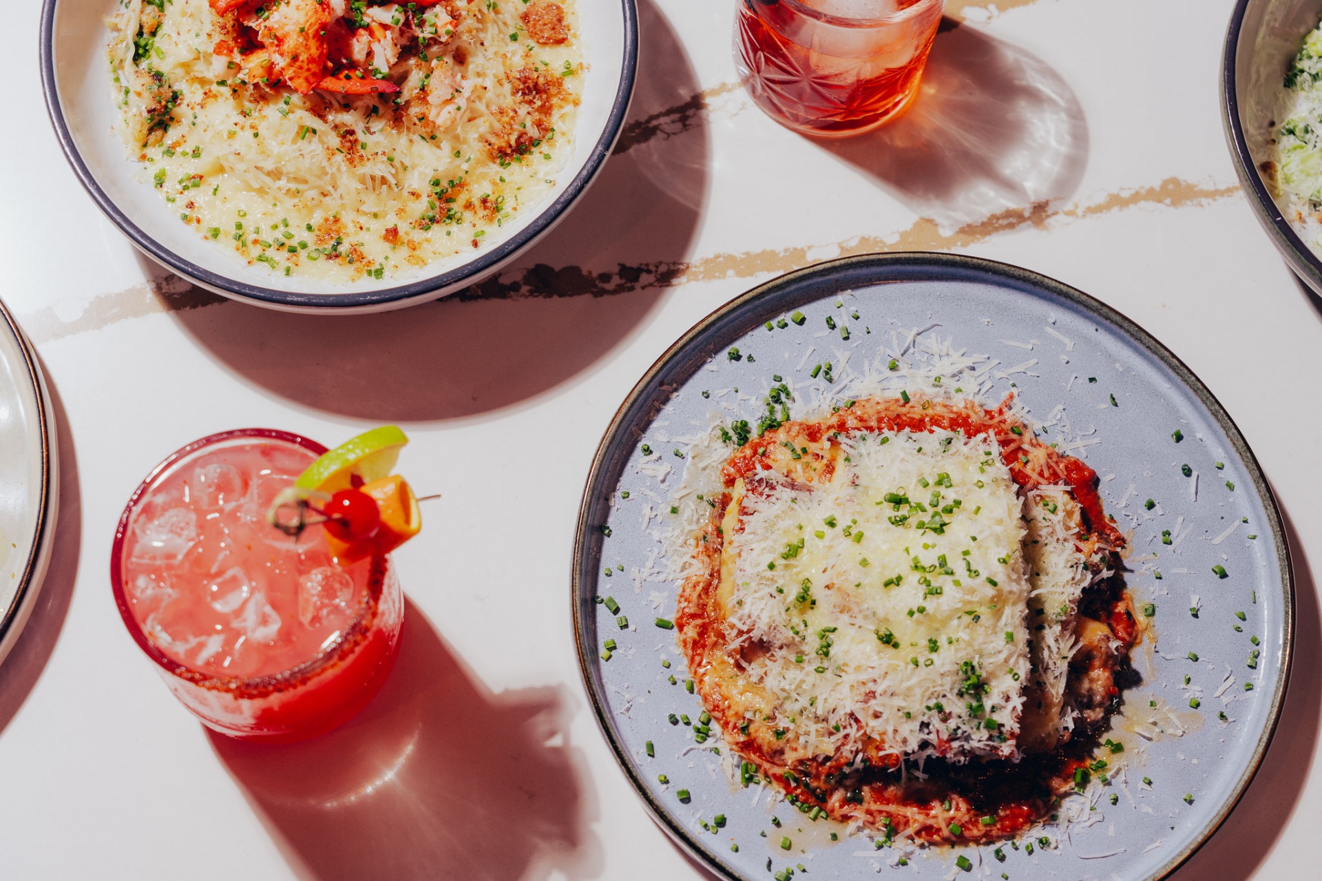 Oxtail lasagna, lobster pasta and cocktails on a marble table at White Wine & Butter